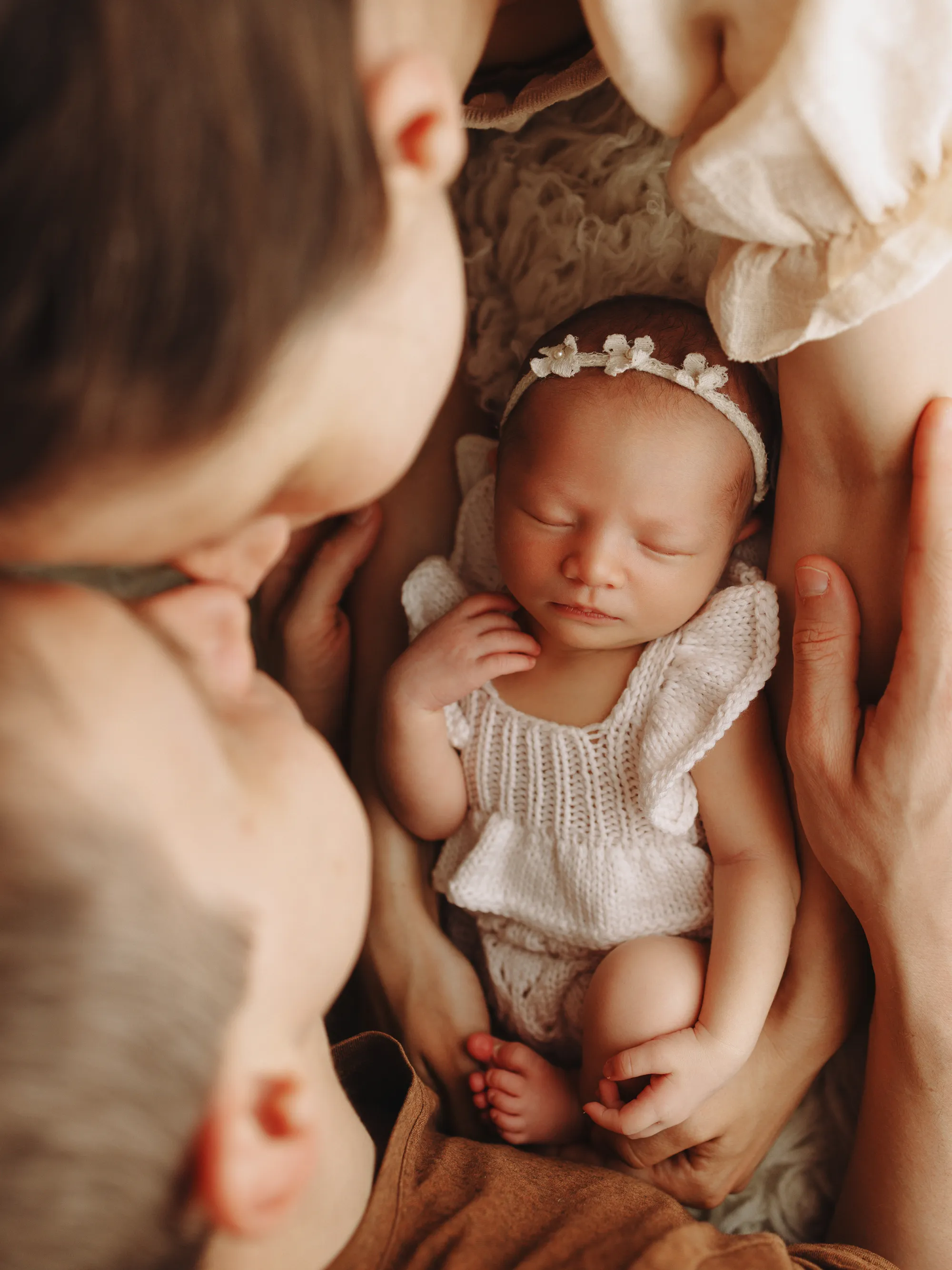 Parents leaning over their newborn daughter in a lace romper and headband