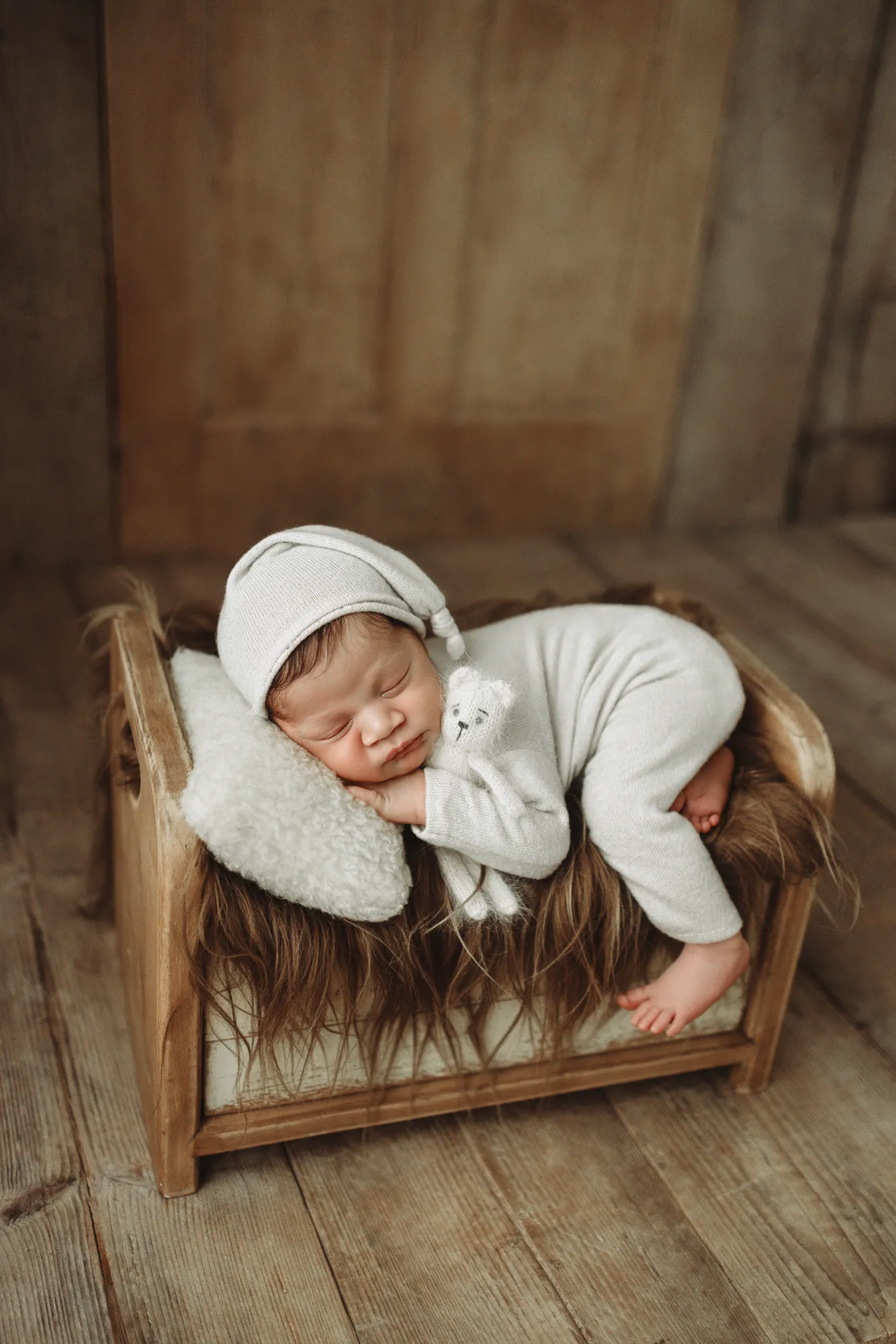 Newborn in a white sleepy hat and romper sleeping on a small wooden bed