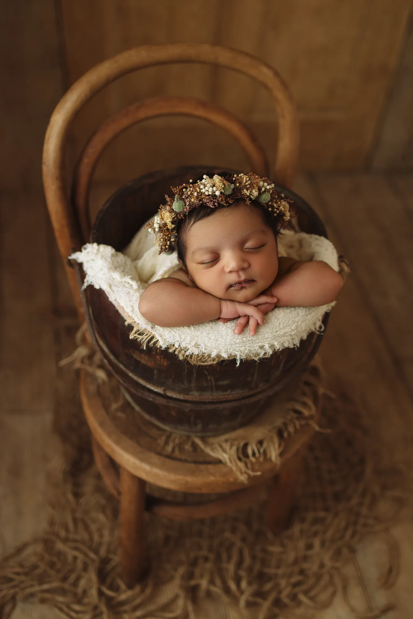 Sleeping newborn in a wooden bucket on a vintage chair, wearing a dried-flower crown