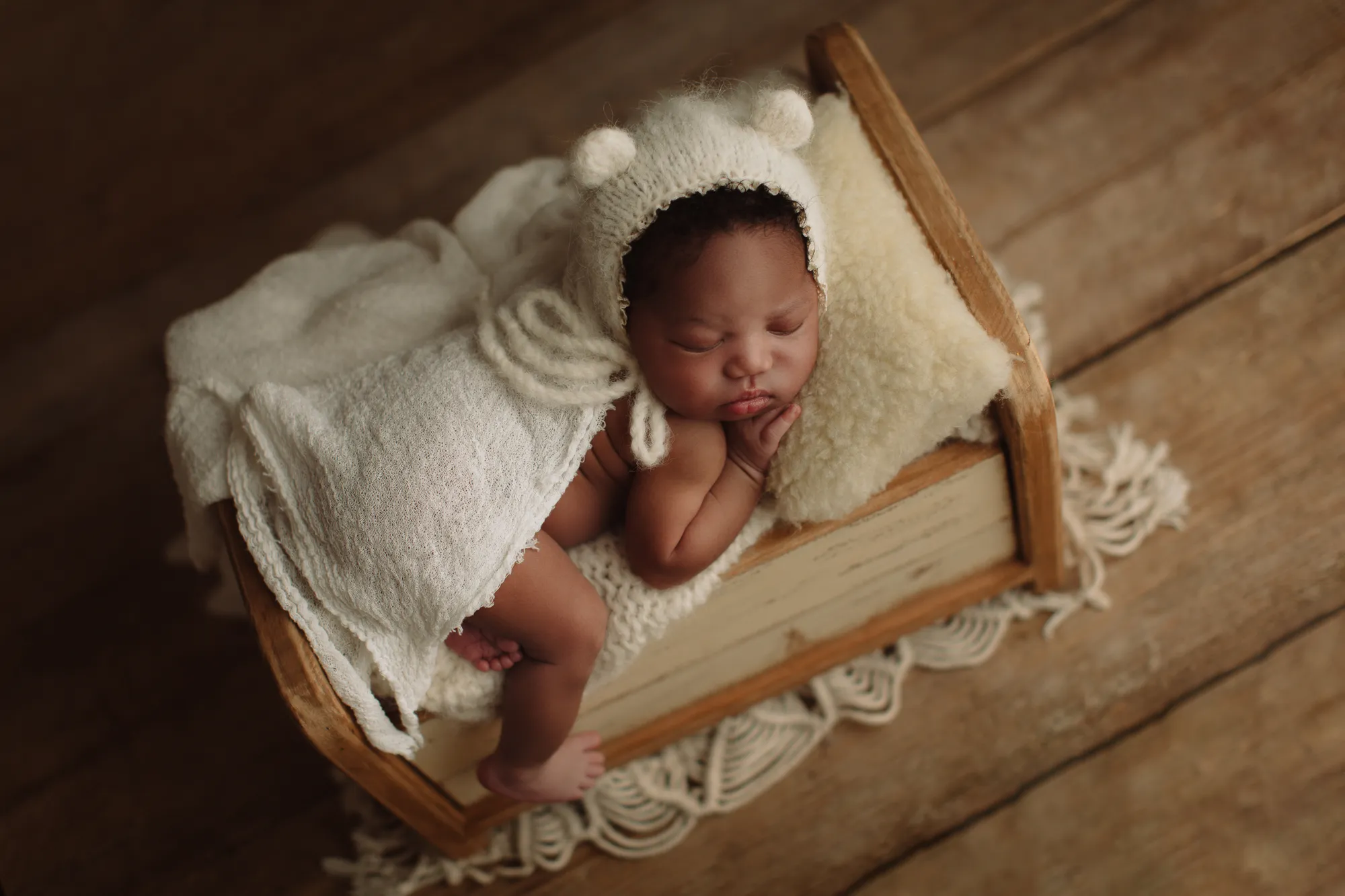 Newborn in a bear-ear bonnet asleep on a small wooden bed