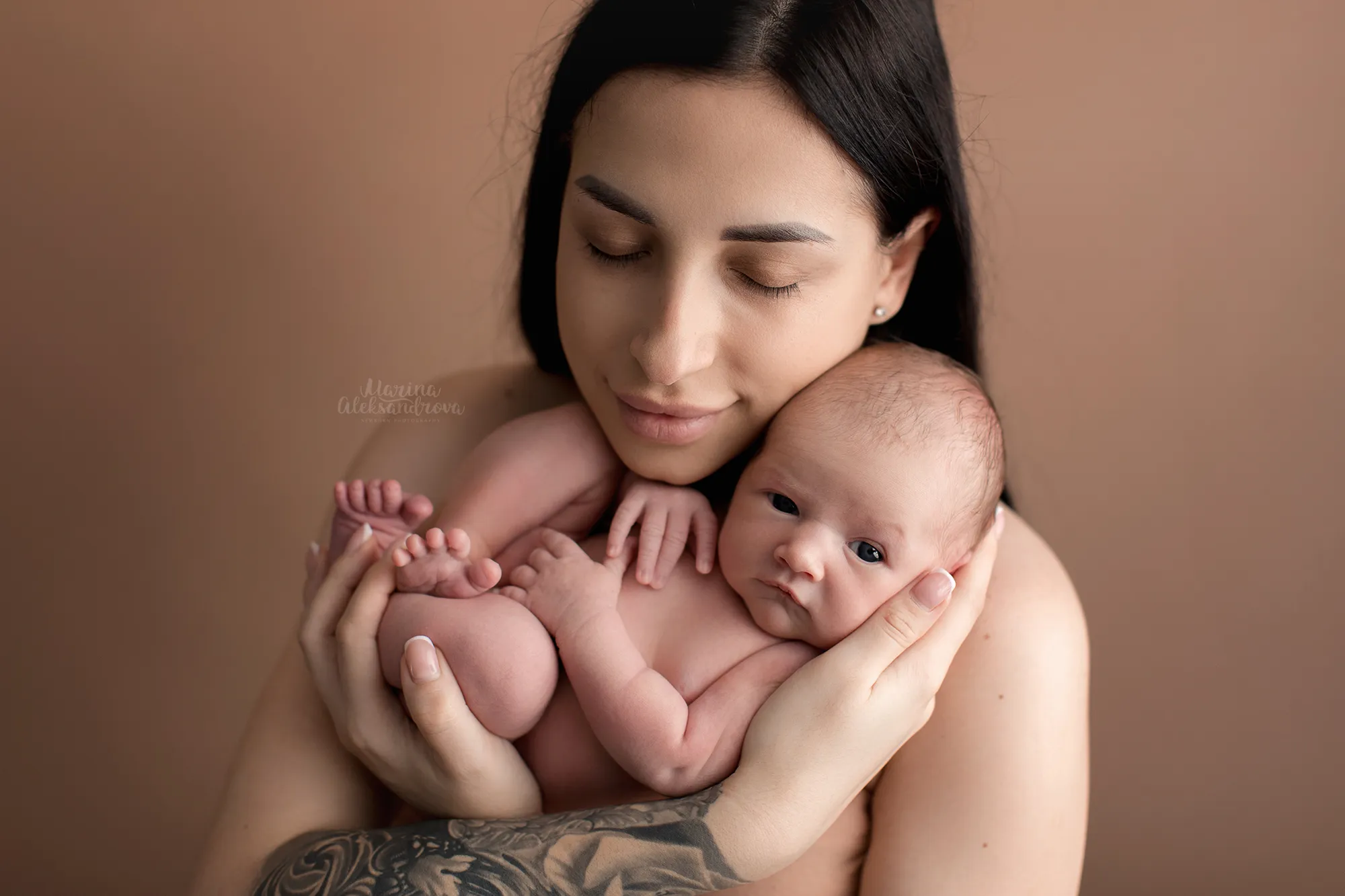 Mother holding her sleeping newborn against her shoulder, brown backdrop