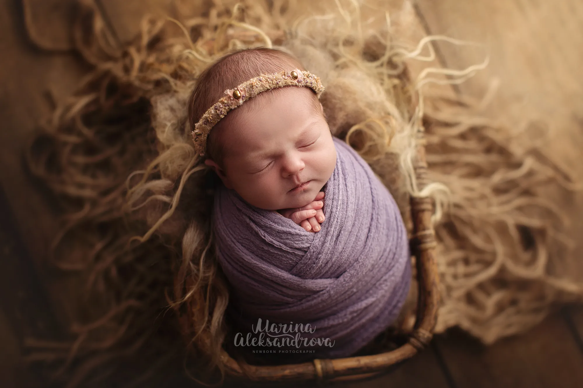 Newborn swaddled in lilac with a floral headband in a basket on jute