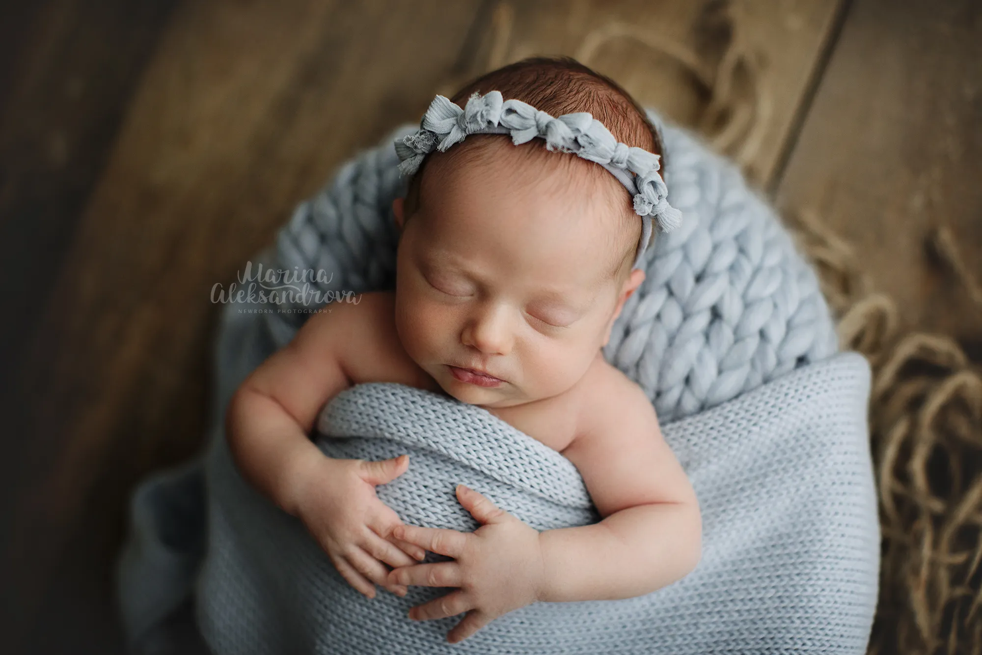 Newborn with a blue floral headband wrapped in a pale blue knit blanket