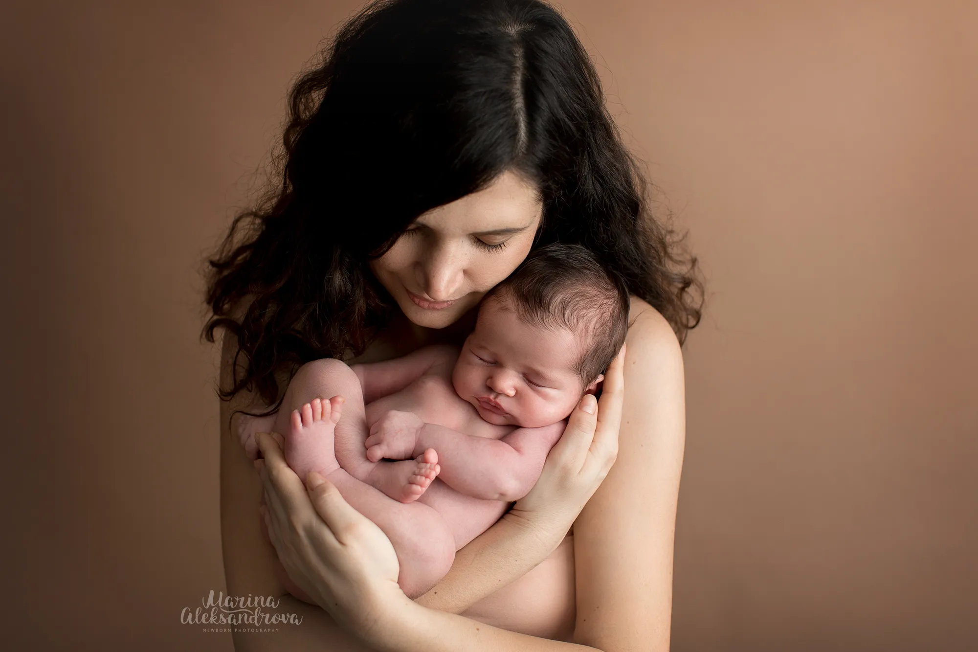 Mother holding her sleeping newborn close against a brown backdrop