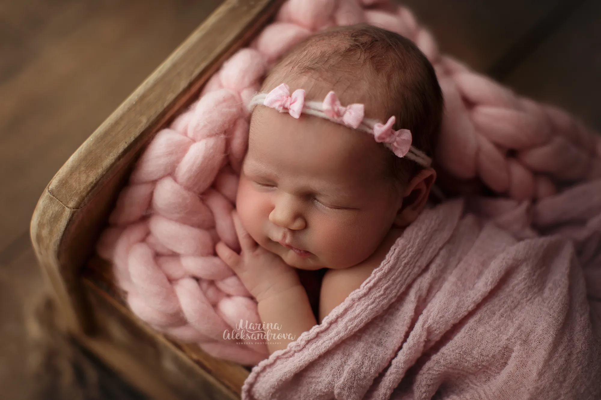 Close-up of a newborn with a pink flower headband on a pink knit blanket