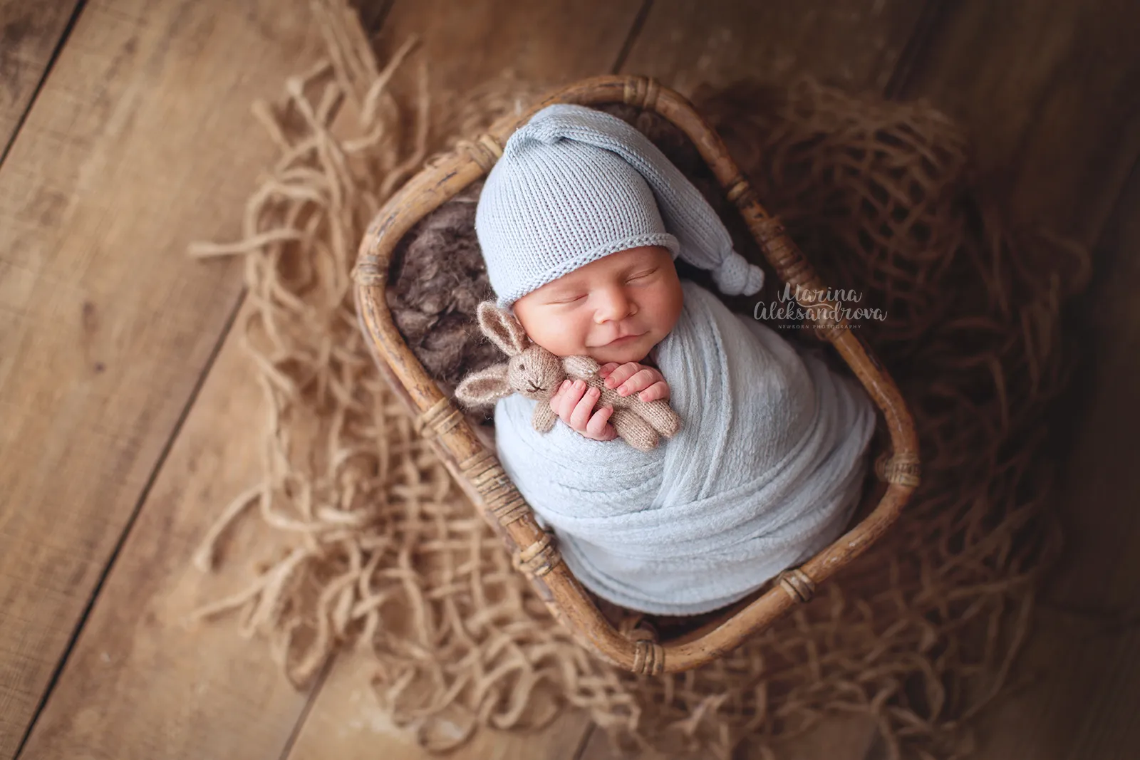 Newborn in a pale blue sleepy hat swaddled in blue with a toy bunny in a basket