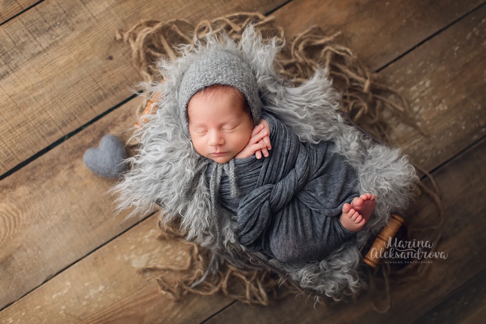 Newborn in a grey bonnet swaddled in grey with a felt heart on grey fur
